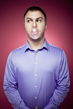 Young man making a chewing gum bubble and looking leftの写真素材