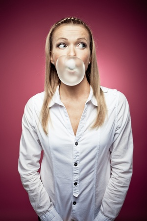 Young woman making a chewing gum bubble and looking rightの写真素材