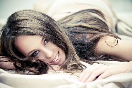 Beautiful lady in lingerie lying in bed of silk sheetsの写真素材