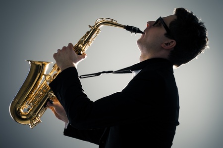 Young man playing sax in the darkの写真素材