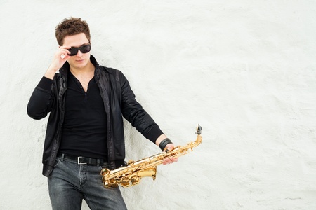 Young man playing sax laening against a wallの写真素材