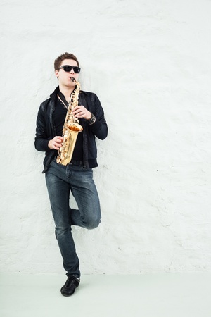 Young man playing sax laening against a wallの写真素材
