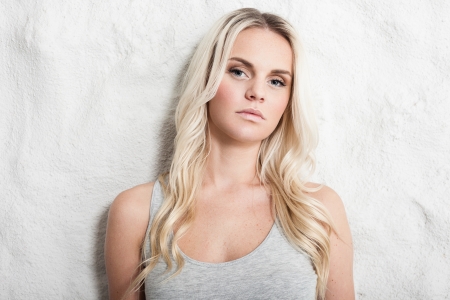 Portrait of a young blond woman leaning on a white wallの写真素材