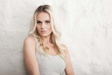 Portrait of a young blond woman leaning on a white wallの写真素材