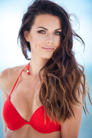 Sexy brunette girl in red swimsuit posing on a beachの写真素材