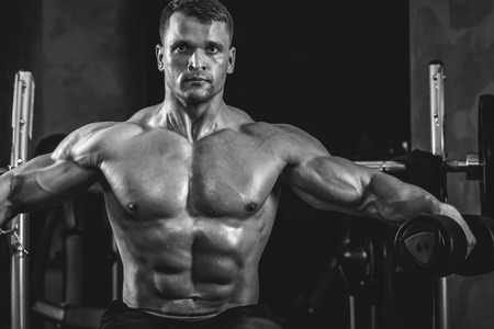 Brutal athletic man pumping up muscles with dumbbells in monochromeの写真素材