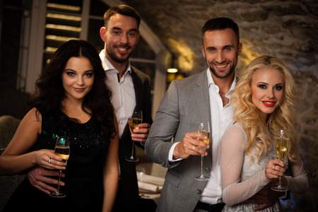 Four friends with champagne glasses celebrating and toasting in restaurantの写真素材