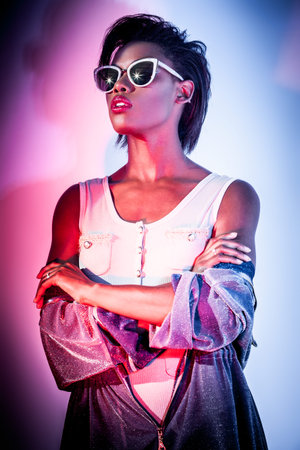 fashion concept - portrait of a beautiful woman in jacket with hood and sunglasses in mixed bright...