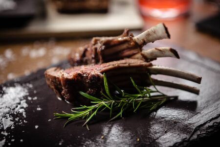 Grilled lamb chops served with a branch of rosemary on a black boardの写真素材