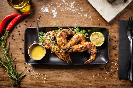 Grilled tiger prawns with chilli sauce and lime served on black plate in restaurantの写真素材