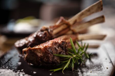 Grilled lamb chops served with a branch of rosemary on a black boardの写真素材