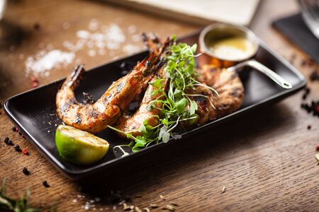 Grilled tiger prawns with chilli sauce and lime served on black plate in restaurantの写真素材