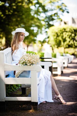 Young woman wearing a hat sitting on a wooden bench and relaxing at the parkの写真素材