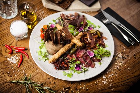 Meat platter for two: Dry-aged beef brisket, duck fillet, beef liver pate, lamb striploin, cranberry jam and grissini. Italian traditional appetizer food closeup served in modern gourmet restaurant.の写真素材