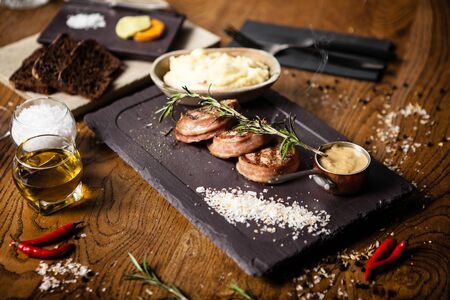 Pork tenderloin with mashed potatos, bacon and mustard sauce with branch of smoking rosemary. Delicious healthy traditional grilled meat food served for lunch in modern cuisine gourmet restaurantの写真素材