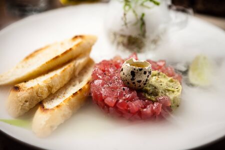 Tuna tartare: Guacamole quail egg baguette on a plate. Delicious healthy raw food closeup served for lunch on a table in modern gourmet cuisine restaurant.の写真素材