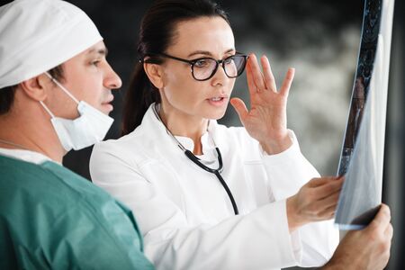 health diagnostic in hospital. male surgeon in mask and female doctor or nurse with stethoscope reviewing x-ray scan results at medical clinicの写真素材