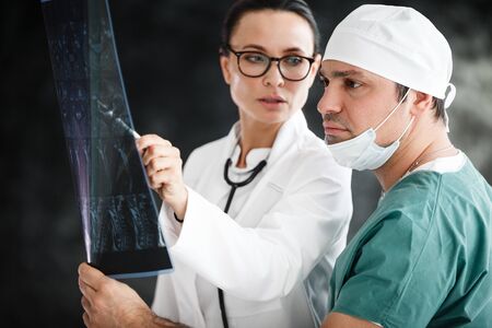health diagnostic in hospital concept. male surgeon in mask and female doctor or nurse with stethoscope reviewing x-ray scan results at medical clinicの写真素材
