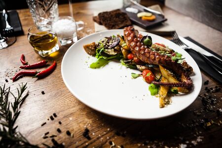 Warm octopus salad with stir fried vegetables and aji sauce on white plate. Delicious healthy mediterranean traditional seafood closeup served on a table for lunch in modern cuisine gourmet restaurantの写真素材