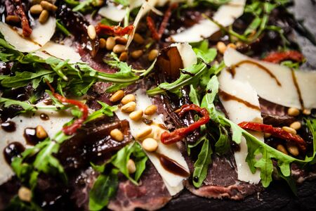 Beef carpaccio with pepper, rucola and parmesan served on a board. Delicious healthy Italian traditional antipasti snacks food closeup served for lunch with wine in modern gourmet cuisine restaurant.の写真素材