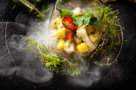 Scallop ceviche with mango, chilli and cilantro served with liquid ice smoke in a plate. Delicious healthy food closeup served for lunch on a table in modern gourmet cuisine restaurant.の写真素材