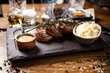 Pork tenderloin with mashed potatos, bacon and mustard sauce with branch of smoking rosemary. Delicious healthy traditional grilled meat food served for lunch in modern cuisine gourmet restaurant.の写真素材