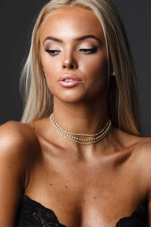Portrait of blond young woman with beautiful makeup and hairstyle in a black lace dress stands on gray background. Fashion model poses in elegant clothes in studioの写真素材