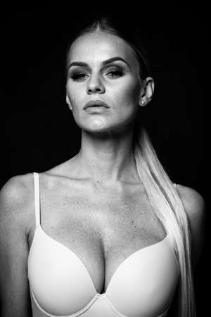 fashion and lingerie concept - beautiful blond lady portrait in sexy nude color corset on black background. Woman wearing underwear poses in studio light. Black and white, monochromeの写真素材