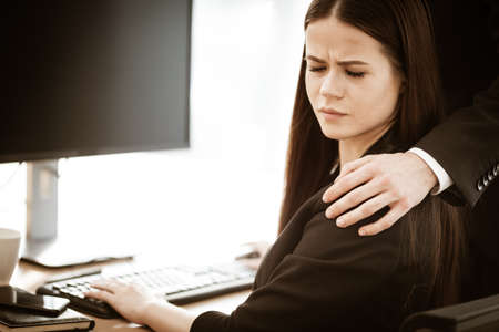 Sexual harassment at work. Male businessman puts hand on annoyed female assistant shoulder at workplace showing inappropriat behaviour. Two people man and woman conflict relations in modern officeの写真素材