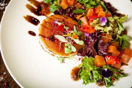 Goat cheese salad. Strawberry-melon salad with chilli, apple-orange sauce, fig jam on white plate. Delicious meat food closeup served on a table for lunch in modern cuisine gourmet restaurantの写真素材