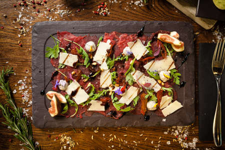 Beef carpaccio with pepper, rucola and parmesan served on a board. Delicious healthy Italian traditional antipasti snacks food closeup served for lunch with wine in modern gourmet cuisine restaurantの写真素材