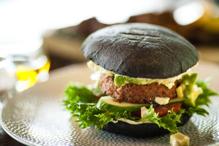 Vegan burger. Black bun, tofu-avocado salad, mayonnaise, cucumber, tomato, fresh salad. Delicious healthy hamburger food closeup served on a table for lunch in modern cuisine gourmet restaurant.の写真素材