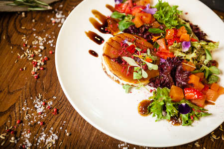 Goat cheese salad. Strawberry-melon salad with chilli, apple-orange sauce, fig jam on white plate. Delicious meat food closeup served on a table for lunch in modern cuisine gourmet restaurantの写真素材