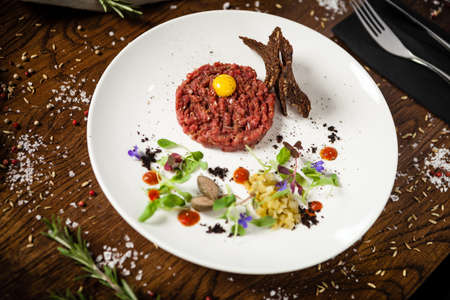 Steak tartare. Horseradish creme, black bread, baguette chips on white plate. Delicious healthy raw meat food closeup served on a table for lunch in modern cuisine gourmet restaurant.の写真素材