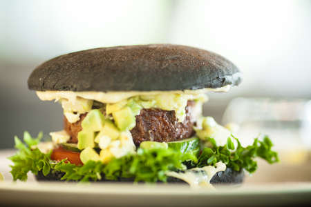 Vegan burger. Black bun, tofu-avocado salad, mayonnaise, cucumber, tomato, fresh salad. Delicious healthy hamburger food closeup served on a table for lunch in modern cuisine gourmet restaurant.の写真素材