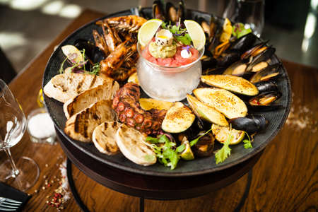 Seafood platter for 2-4 persons. Octopus, blue mussels, cooked green mussels, grilled tiger prawns, tuna tartare. Delicious seafood closeup served on a table for lunch in modern gourmet restaurantの写真素材