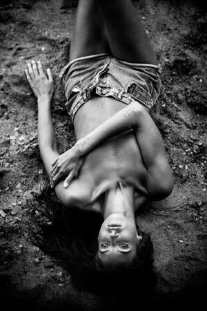 Summertime recreation concept. Beautiful young sexy woman with fit trained slim body wearing blue shorts lies on a beach. Fashion female model poses by the sea. Black and white monochrome.の写真素材