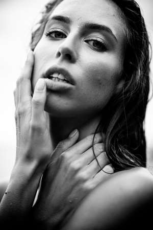 Summertime recreation concept. Beautiful young sexy woman with fit trained slim body and wet hair closeup portrait on a beach. Fashion female model poses by the sea. Black and white monochrome.の写真素材