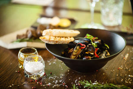 Blue mussels in white wine sauce in black bowl. Delicious healthy seafood closeup served on a table for lunch in modern cuisine gourmet restaurantの写真素材