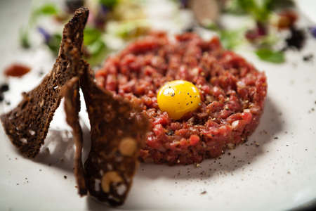 Steak tartare. Horseradish creme, black bread, baguette chips on white plate. Delicious healthy raw meat food closeup served on a table for lunch in modern cuisine gourmet restaurant.の写真素材