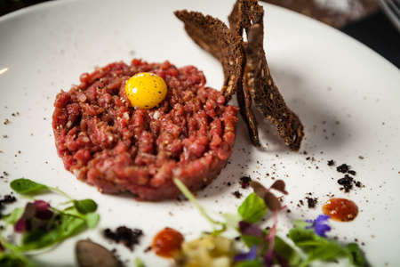 Steak tartare. Horseradish creme, black bread, baguette chips on white plate. Delicious healthy raw meat food closeup served on a table for lunch in modern cuisine gourmet restaurant.の写真素材