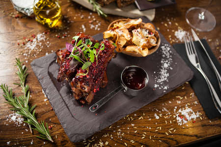 Pork ribs cooked at low temperature. Blackcurrant sauce, parsnip chips with Parmesan cheese. Delicious healthy meat food closeup served on a table for lunch in modern cuisine gourmet restaurantの写真素材