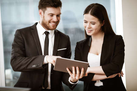 Successful business and modern technology concept. Young businesswoman and happy smiling businessman working together using tablet computer. Two colleagues man and woman teamwork indoors.の写真素材