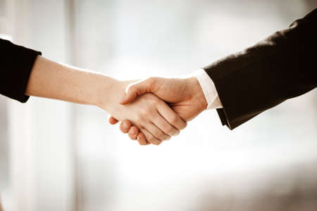 Successful business concept. Young businesswoman and businessman shake hands closeup after signing partnership cooperation contract in office. Two managers man and woman teamwork indoors.の写真素材