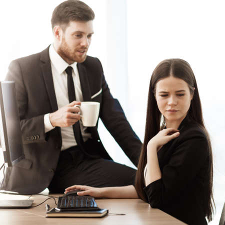Sexual harassment at work. Male businessman sits and flirts with annoyed female assistant at workplace showing inappropriat behaviour. Two people man and woman conflict relations in modern officeの写真素材