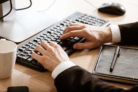 Business and technology concept. Businessmans sits at office table with hands lying on desktop computer keyboard closeup. Distance learning, education online. Working from home.の写真素材