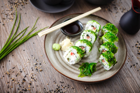 Sushi maki rolls with cucumber, avocado, tomato, creamy cheese, chuka wakame on a plate with chopsticks, soy sauce, wasabi and ginger. Japanese traditional seafood served for lunch in restaurant.の写真素材