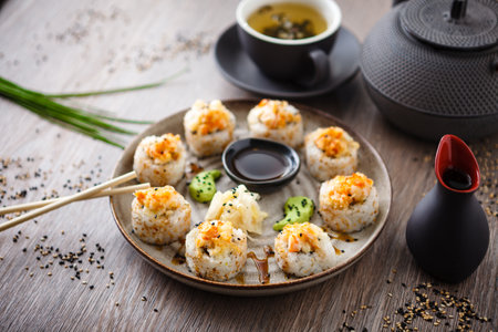 Baked sushi maki rolls with prawns and crab on a plate with chopsticks, soy sauce, wasabi and ginger. Japanese traditional fish food closeup served for lunch in modern gourmet restaurant.の写真素材