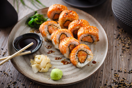 Baked sushi maki rolls with salmon, crab and spicy sauce on a plate with chopsticks, soy sauce, wasabi and ginger. Japanese traditional fish food closeup served for lunch in modern gourmet restaurant.の写真素材