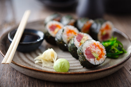 Sushi maki rolls with tuna, flying fish caviar, crab, avocado on a plate with chopsticks, soy sauce, wasabi and ginger. Japanese traditional food closeup served for lunch in modern gourmet restaurant.の写真素材